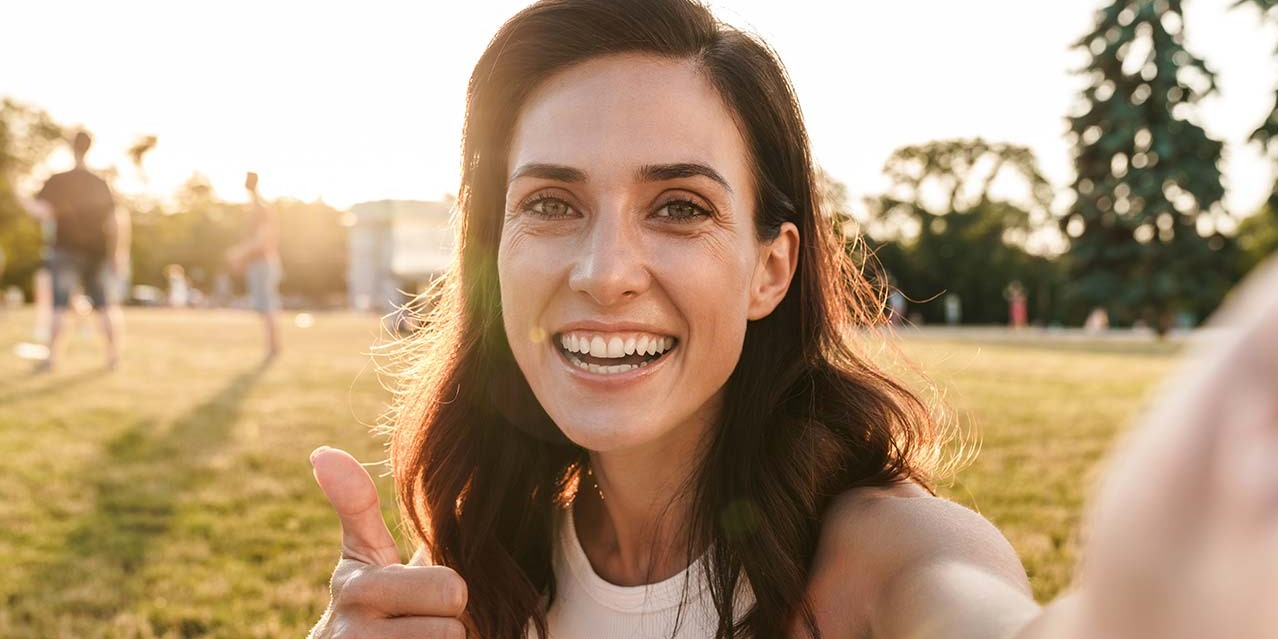 Lächelnde Frau im Park zeigt einen Daumen nach oben