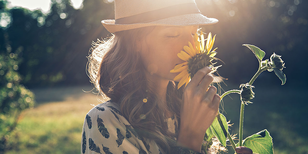 Frau mit Hut riecht an einer Sonnenblume