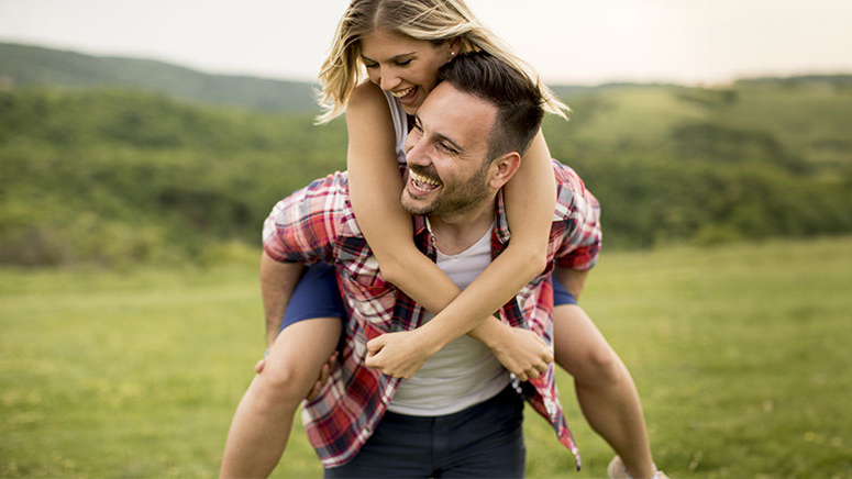 Mann trägt Frau auf seinem Rücken über eine grüne Wiese