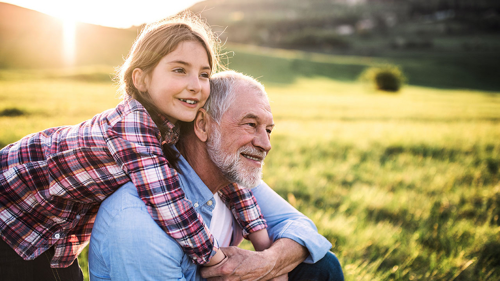 Glückliche Enkeltochter umarmt ihren Opa auf einer Wiese
