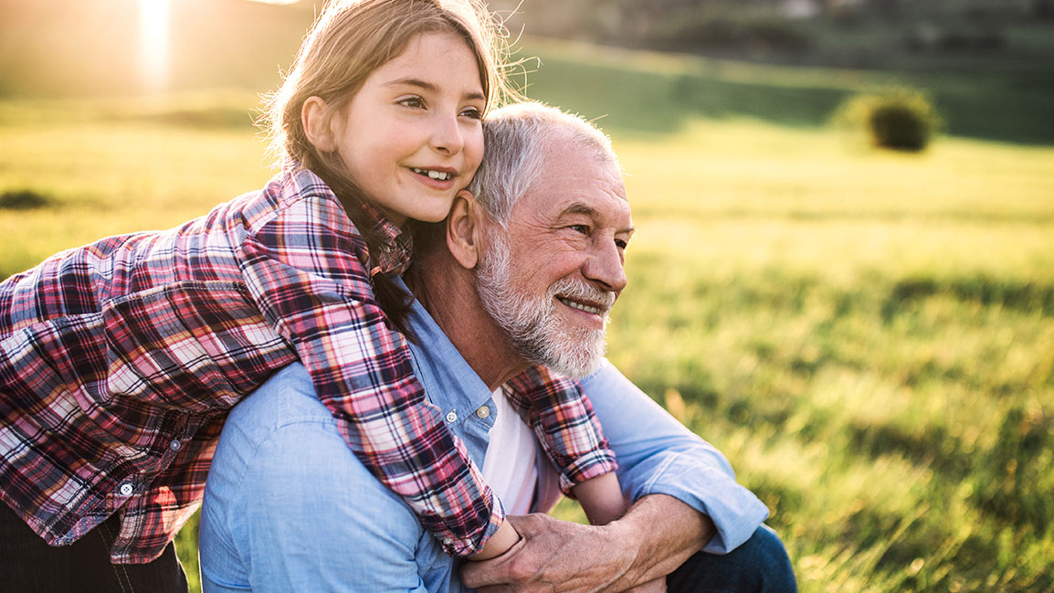 Kinder & Enkel unterstützen Glückliche Enkeltochter umarmt ihren Opa auf einer Wiese