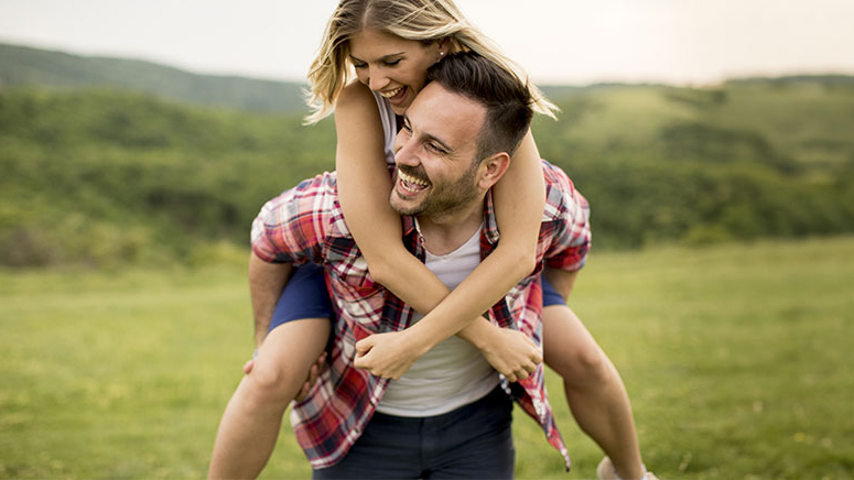 Mann trägt Frau auf dem Rücken auf einer grünen Wiese