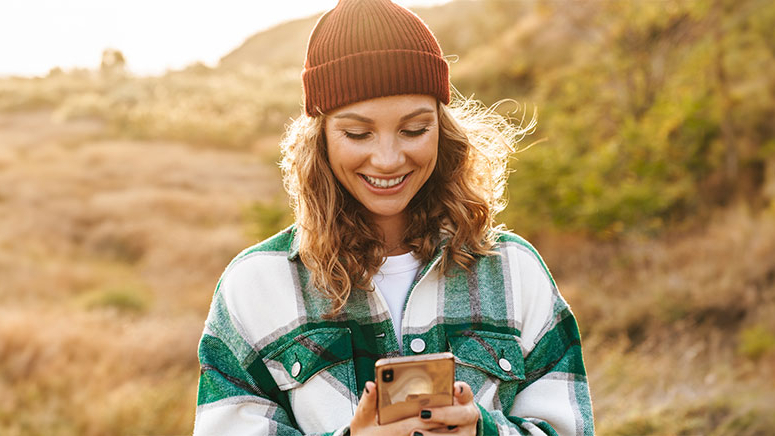 Junge Frau schaut beim Spazierengehen auf ihr Handy