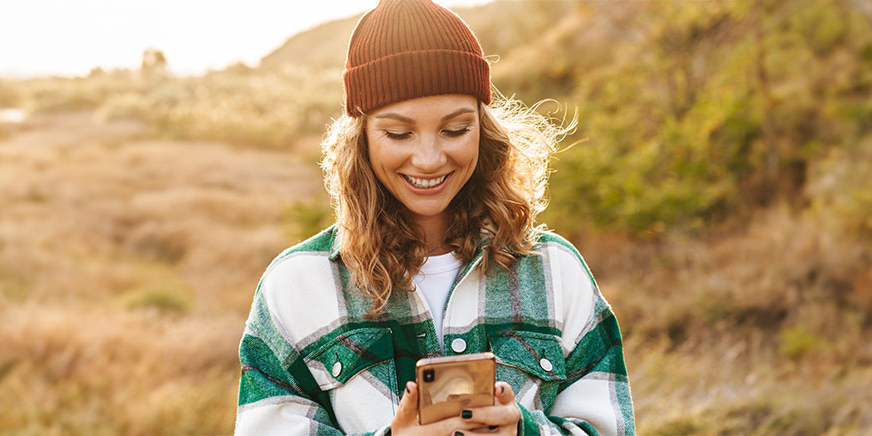 Junge Frau schaut beim Spazierengehen auf ihr Handy