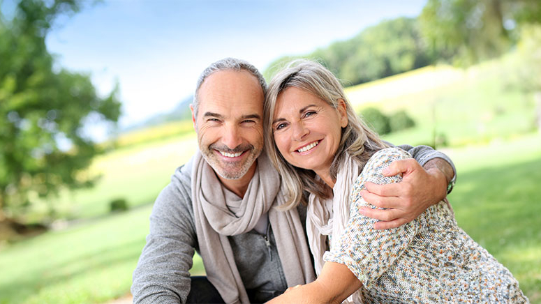 Lächelndes älteres Pärchen umarmt sich auf einer Wiese