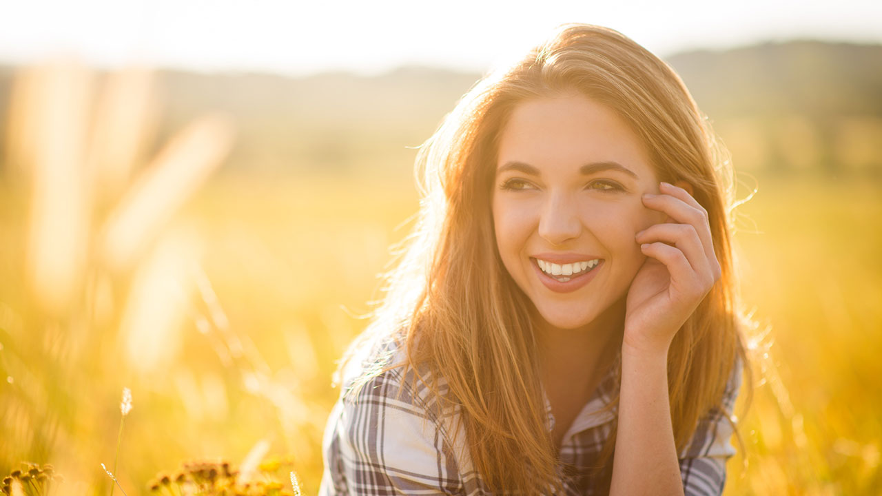 Lächelnde junge Frau sitzt in einem Feld