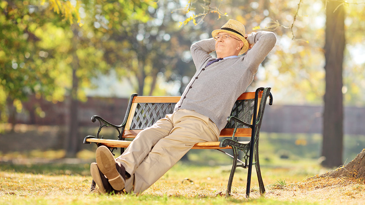 Älterer Mann mit Hut sitzt auf einer Parkbank