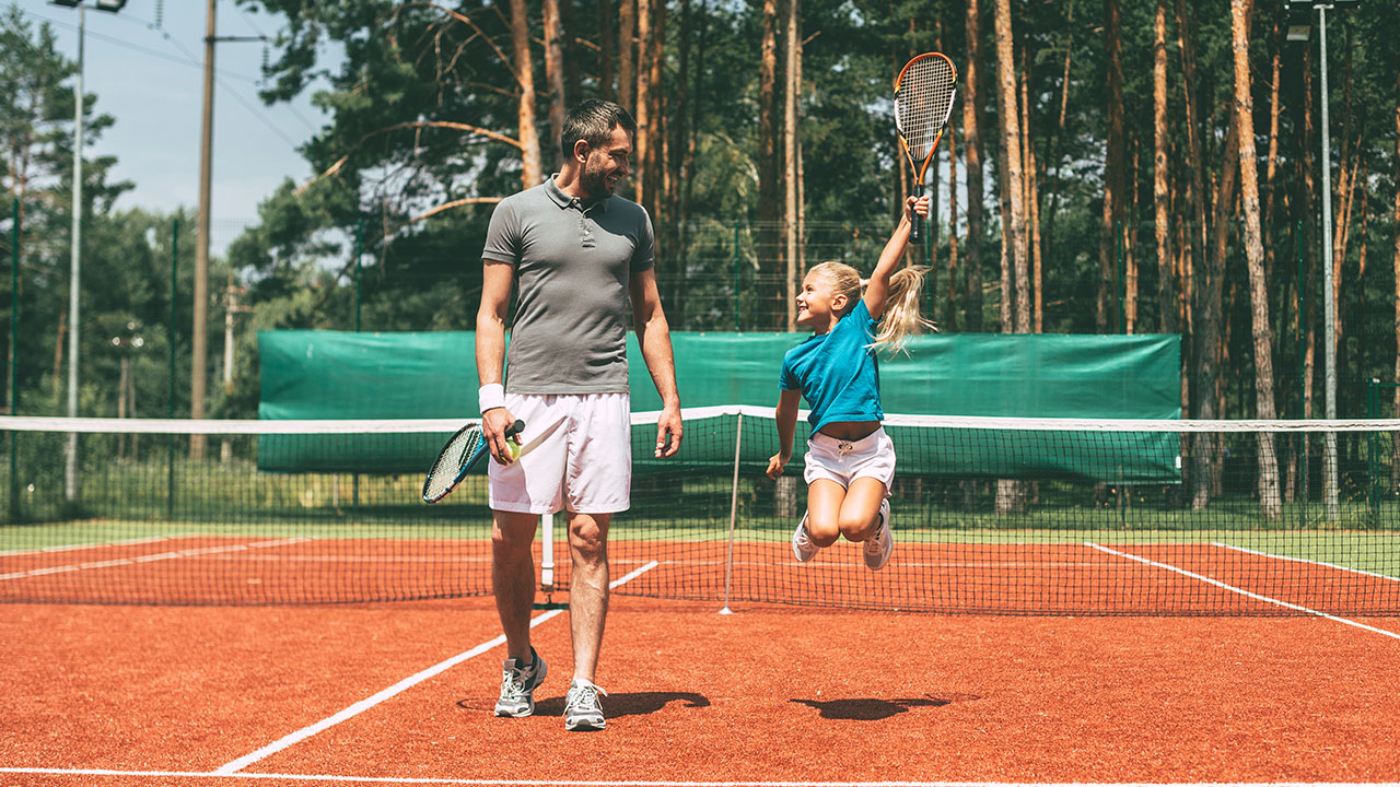 Vater und Tochter mit Tennisschlägern auf Tennisplatz
