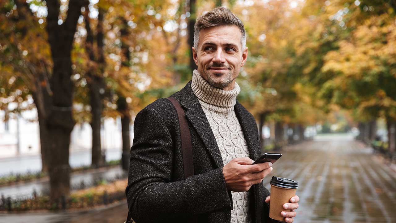 Investmentdepot eröffnen Mann mit Smartphone und Coffee-to-Go läuft Straße entlang