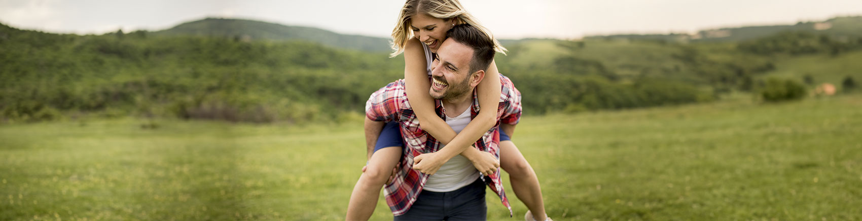 Mann trägt Frau auf dem Rücken auf einer grünen Wiese