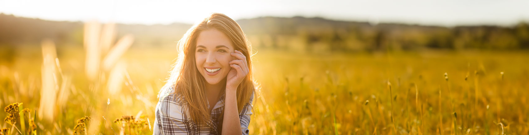 Lächelnde junge Frau sitzt in einem Feld