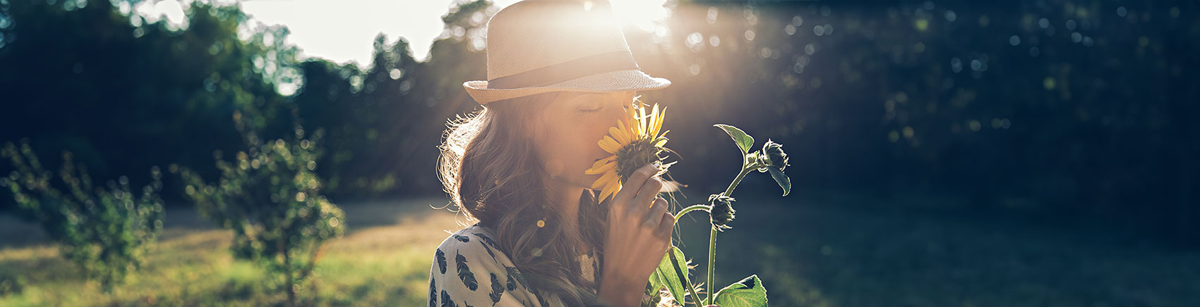 Frau mit Hut riecht an einer Sonnenblume