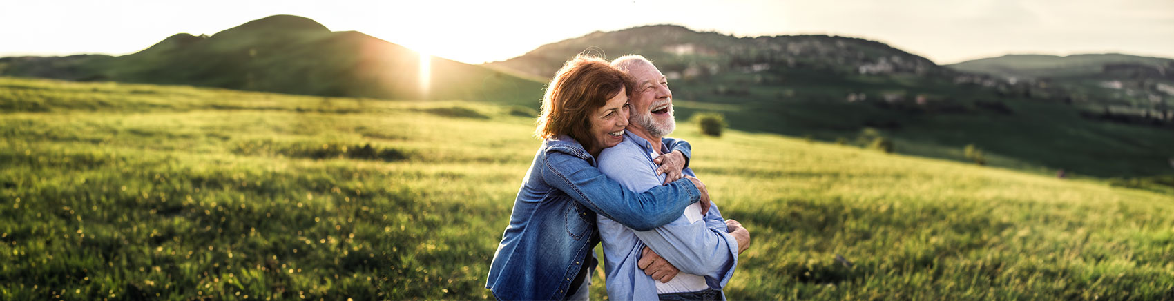 Lächelndes älteres Pärchen umarmt sich auf einer Wiese