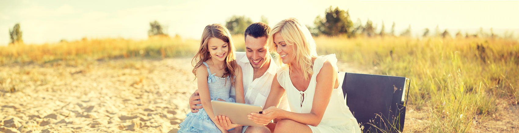 Familie sitzt am Strand und schaut gemeinsam in ein Tablet