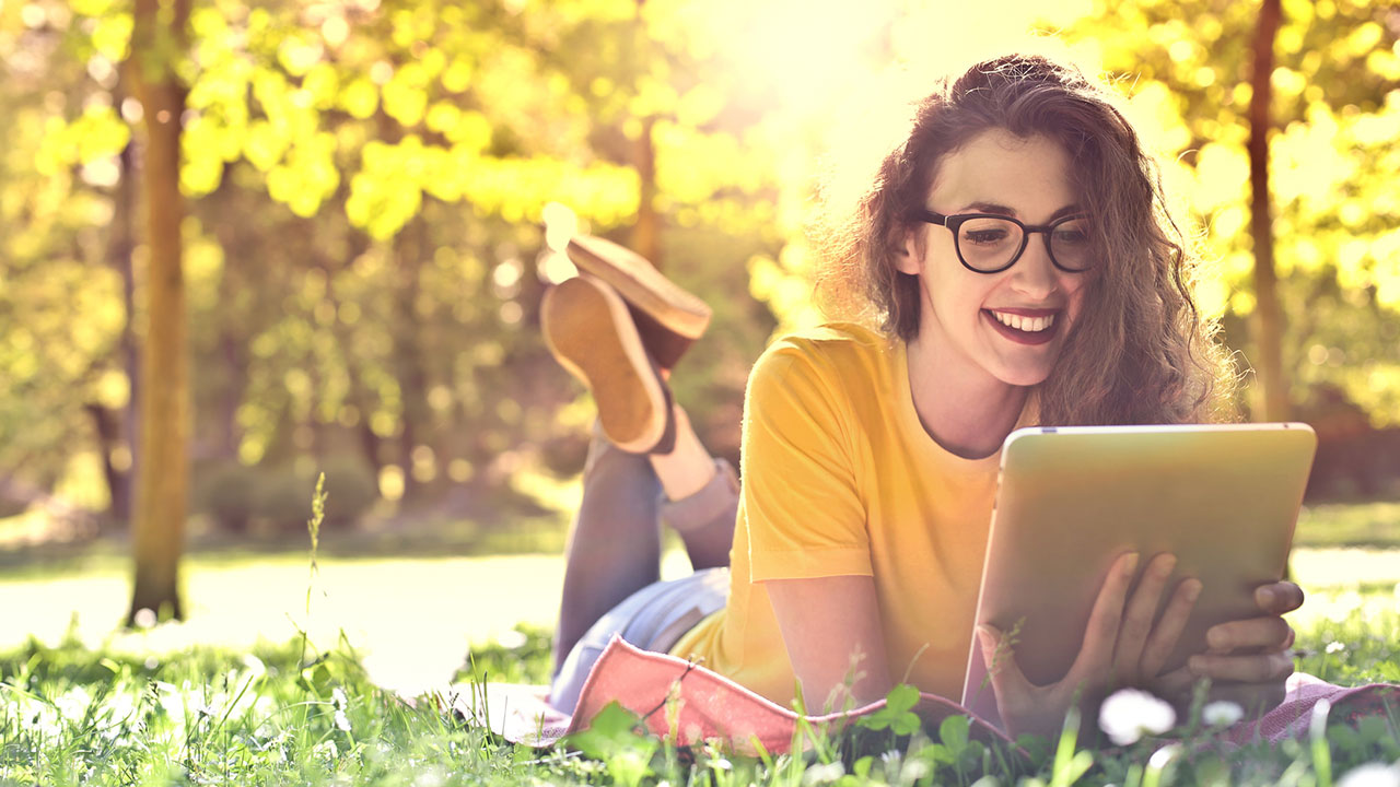 Junge Frau liegt auf der Wiese und lernt mit Ihrem Tablet