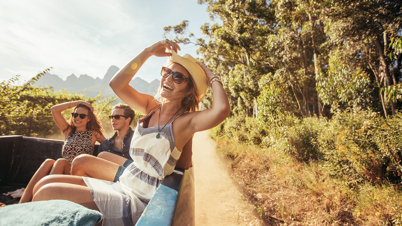 Gruppe junger Menschen sitzt auf der Ladefläche eines Trucks und fährt durch die Natur